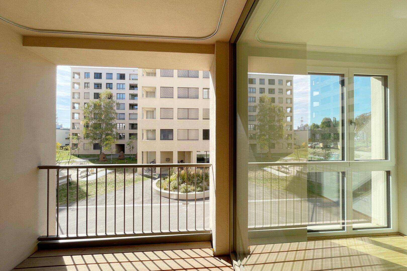 Blick vom Balkon auf den begrünten Innenhof und die umliegenden modernen Wohngebäude.