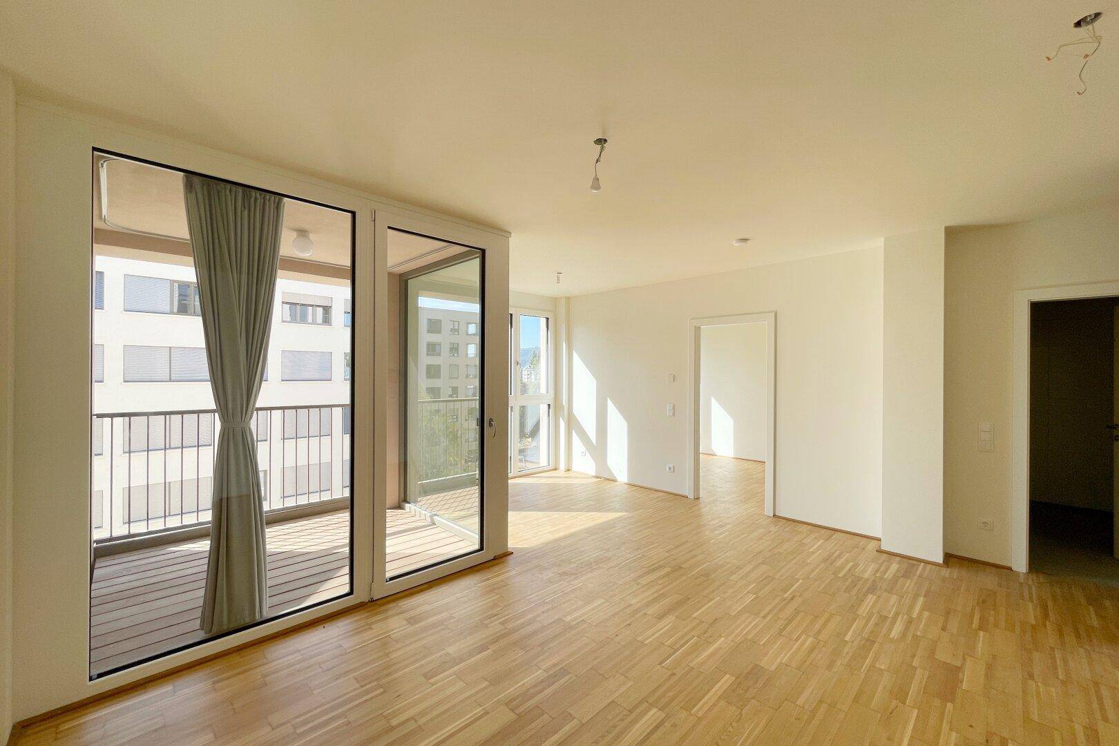 Heller Wohnraum mit Parkettboden und großen Schiebetüren, die auf einen sonnigen Balkon führen.