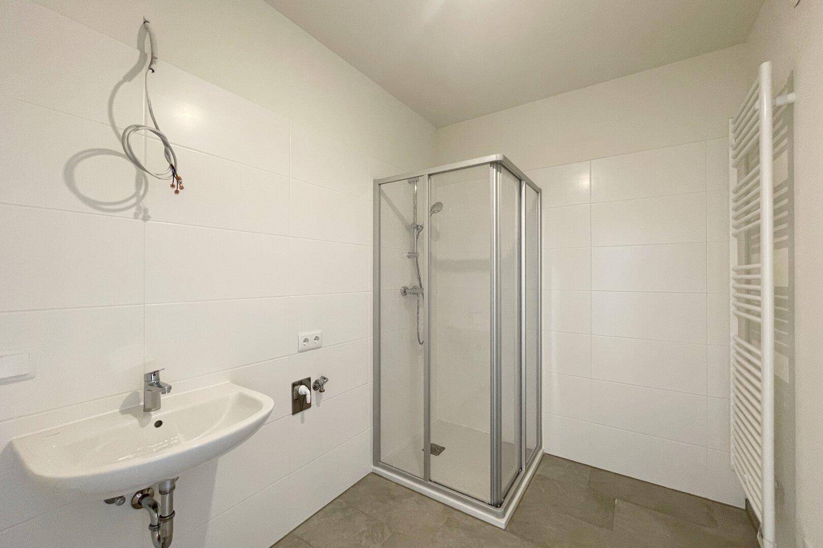 Modernes Badezimmer mit weiß gefliesten Wänden, Duschkabine und beheiztem Handtuchhalter.