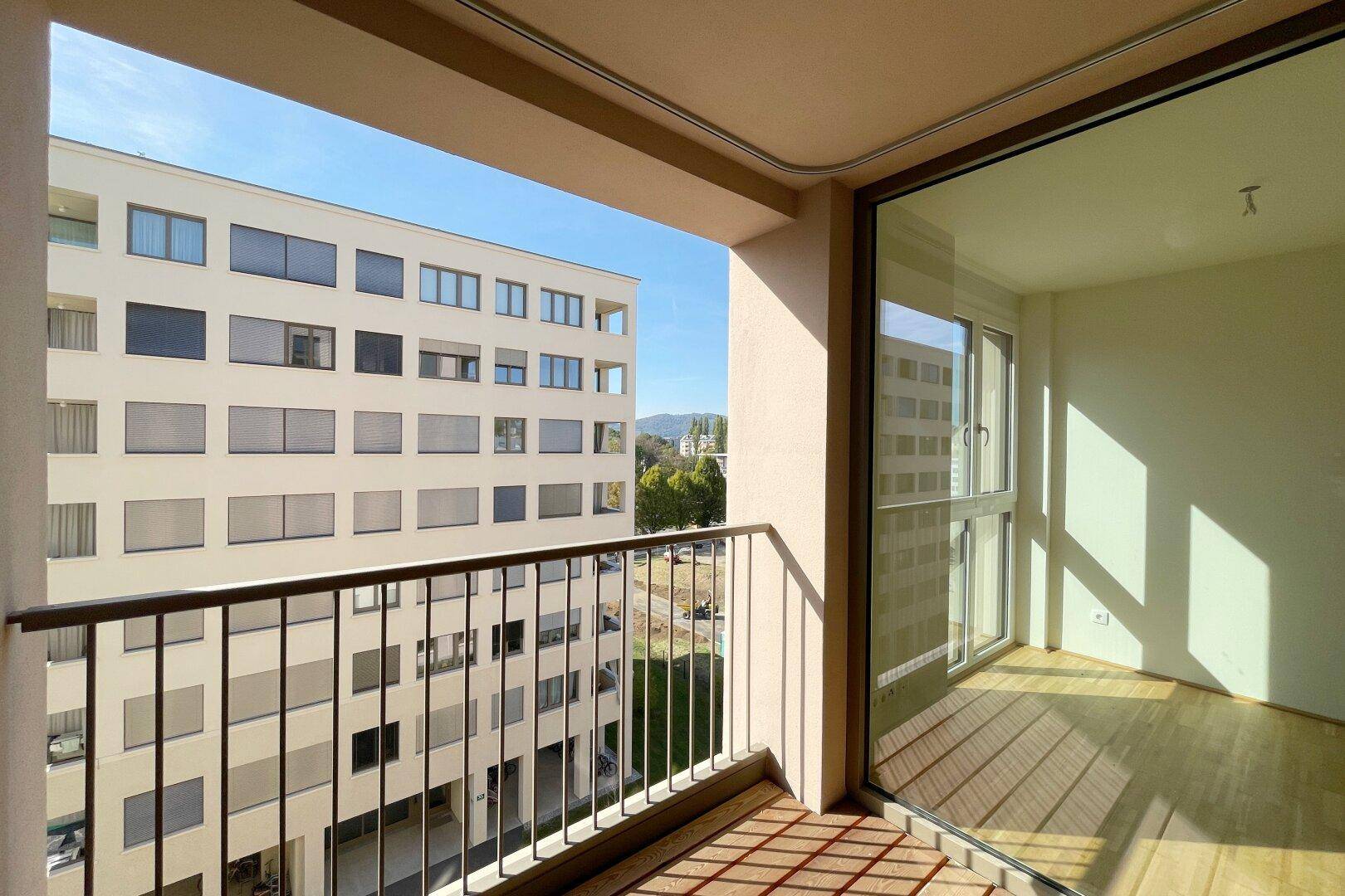Sonnenverwöhnter Balkon mit Holzboden und Blick auf die moderne Architektur der Nachbargebäude.