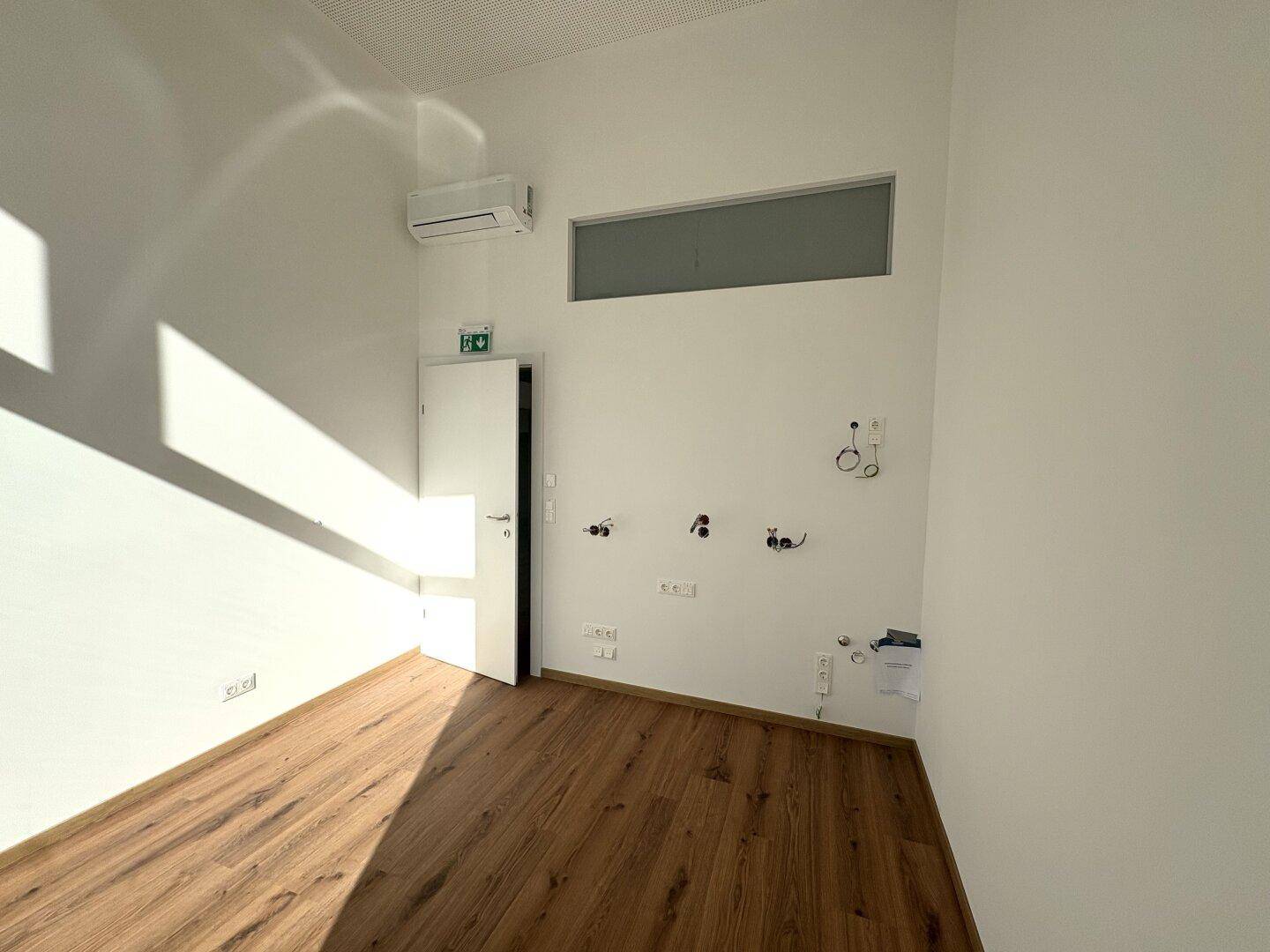 Kleiner Raum mit Laminatboden, Klimaanlage und Anschlüssen für Sanitär und Elektrik, bereit für Installationen.