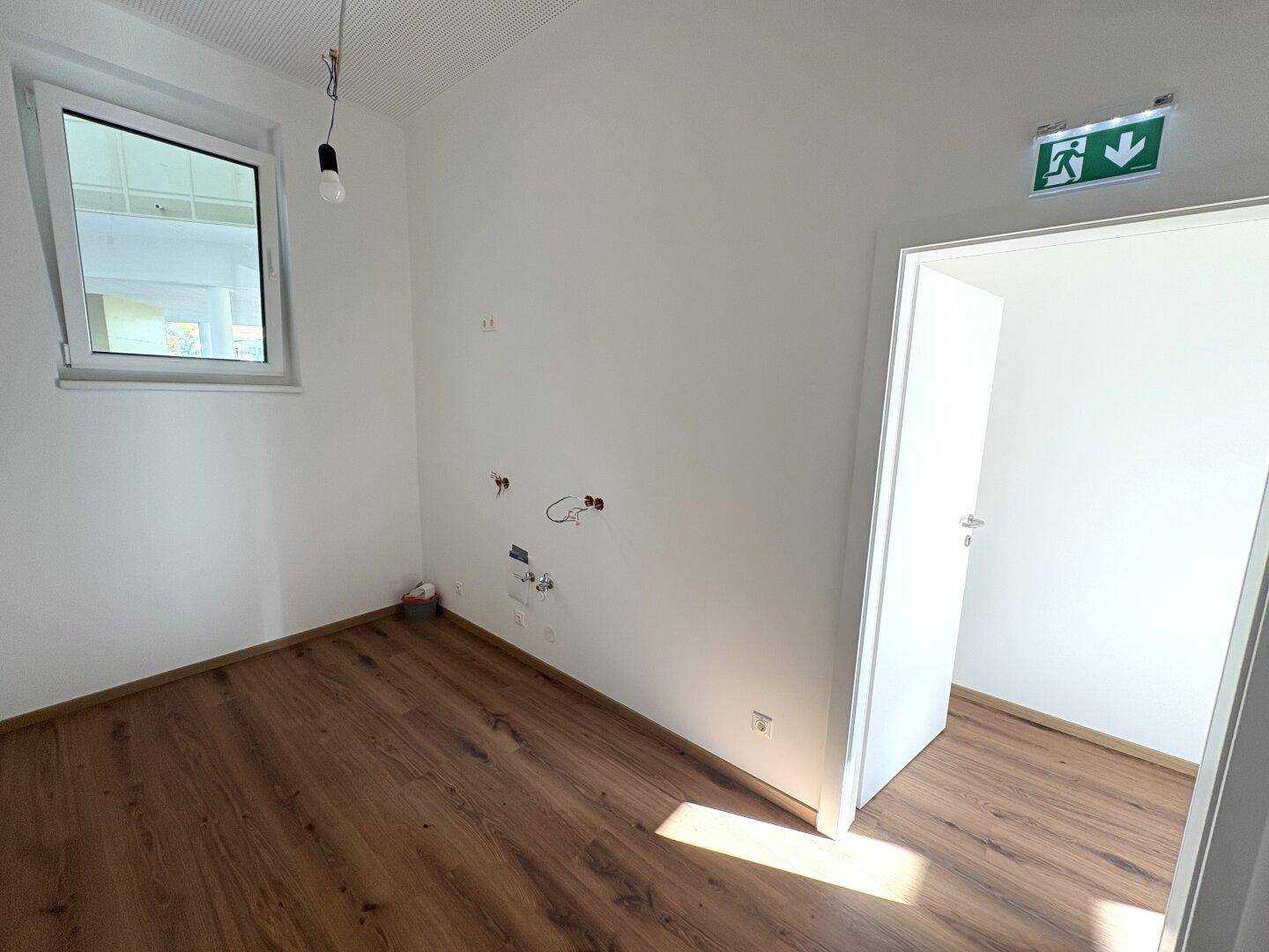 Heller Raum mit Laminatboden, Tür und Fenster, ausgestattet mit Klimaanlage und vorbereiteten Anschlüssen.