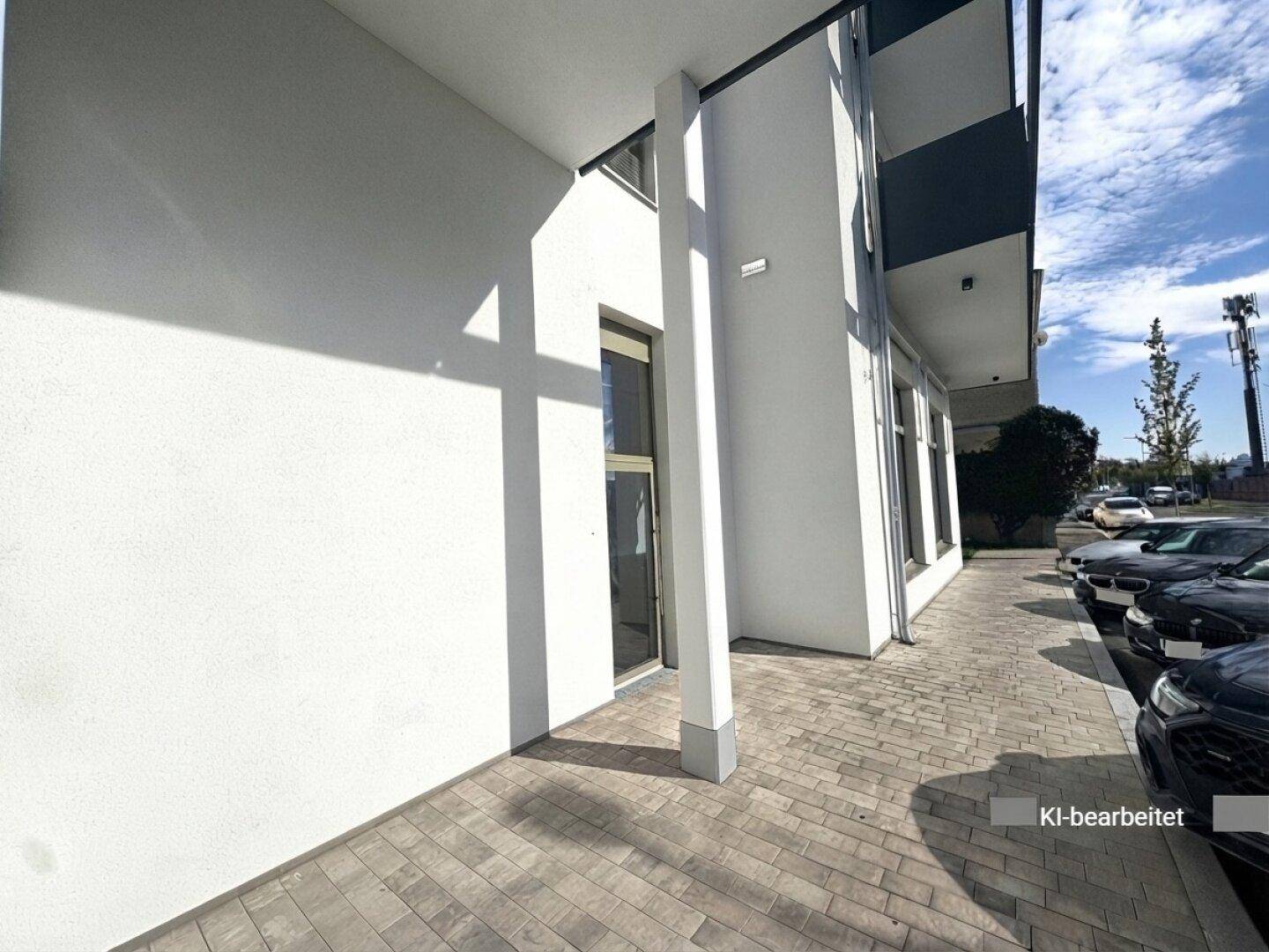 Seitenansicht des modernen Gebäudes mit Eingangstür und großen Fenstern, angrenzend an einen Parkplatz.