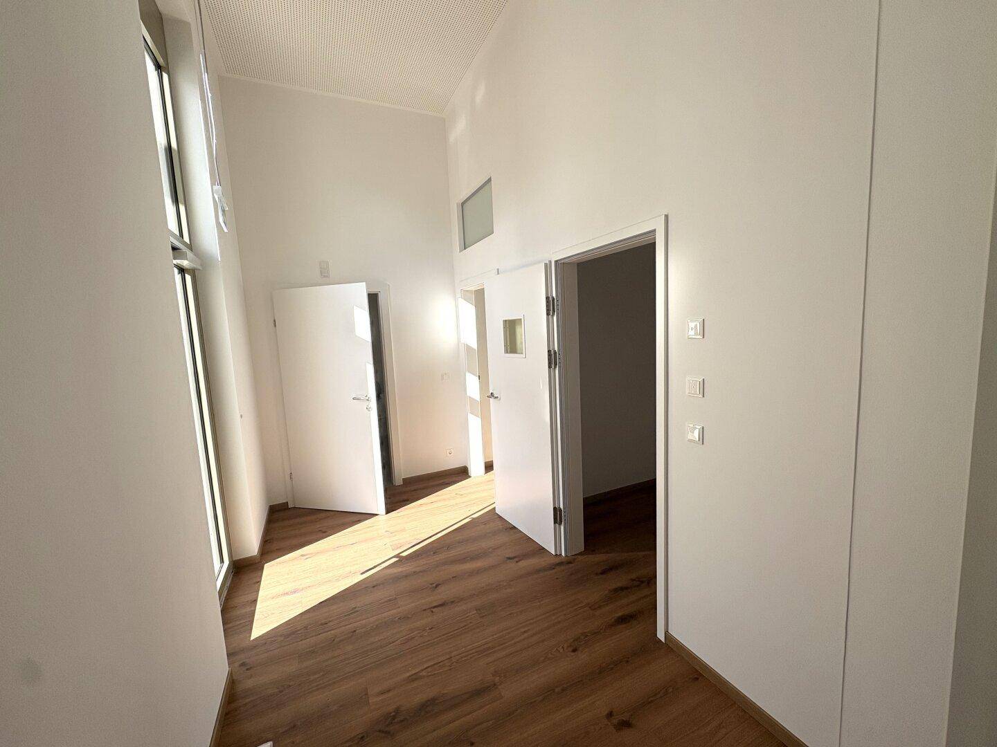 Heller Flur mit Laminatboden und mehreren Türen, durchflutet von natürlichem Licht eines hohen Fensters.