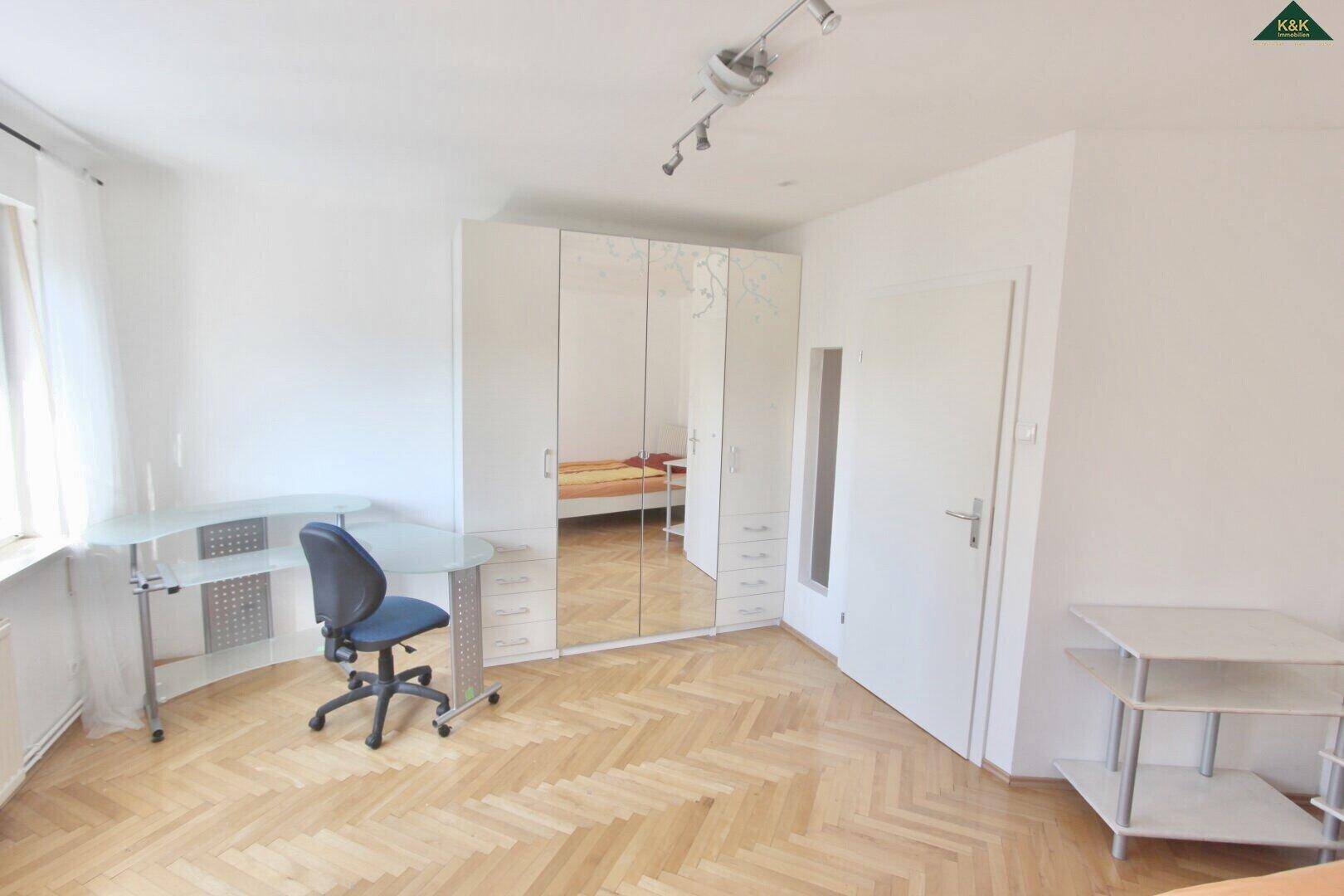 Helles Schlafzimmer mit Fischgrätparkett, großem Spiegelschrank und modernem Arbeitsbereich am Fenster.