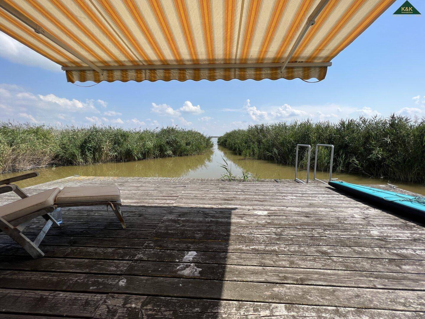 Weitläufiger Holzsteg mit Sonnenliege und Paddleboard, bietet einen weiten Blick über den Wasserkanal.