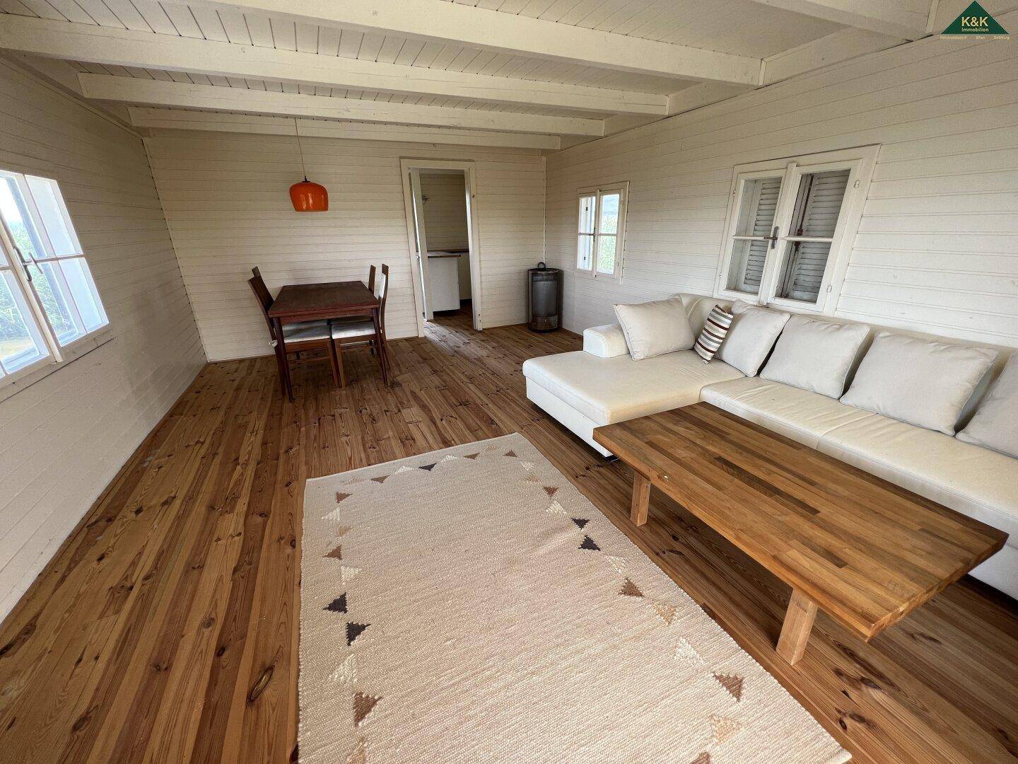 Gemütlicher Wohn- und Essbereich mit Holzboden, weißem Sofa und einem Holztisch, hell und einladend.