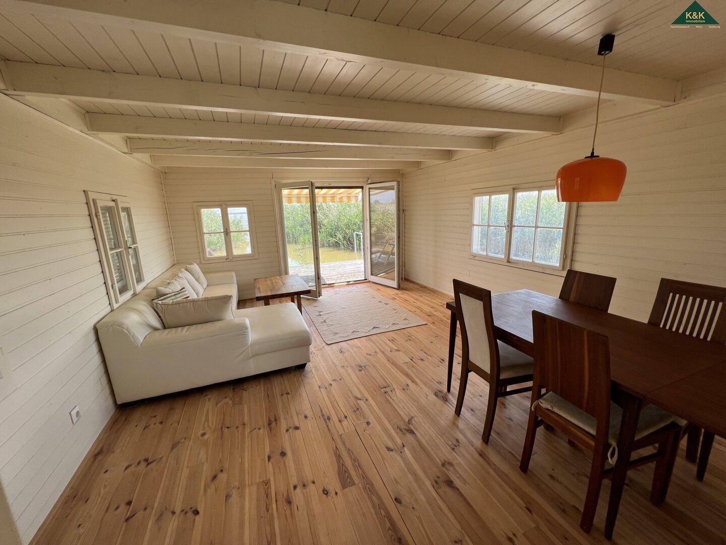 Kombinierter Wohn- und Essbereich mit Holzboden, weißem Sofa und Esstisch, mit Zugang zur Terrasse.