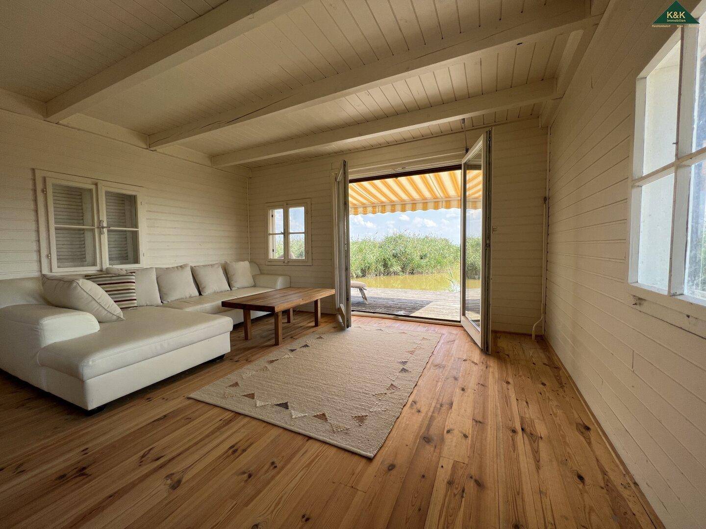 Helles Wohnzimmer mit weißem Sofa, Holzboden und großen Türen mit direktem Blick auf das Wasser.