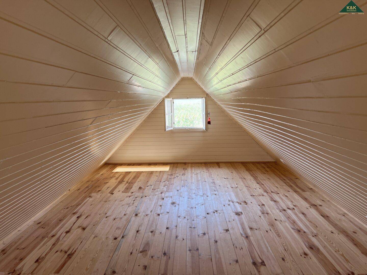 Leerer Dachbodenraum mit schrägen Holzwänden und -decken, ideal für ein weiteres Schlafzimmer oder Stauraum.