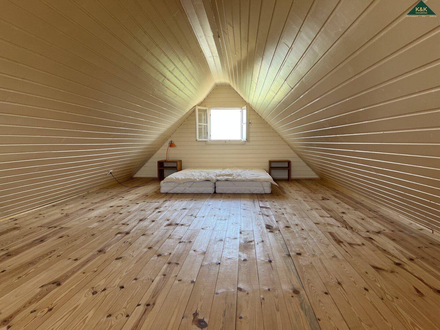 Gemütliches Schlafzimmer im Dachgeschoss mit schrägen Holzwänden, Holzboden und einem kleinen Fenster.
