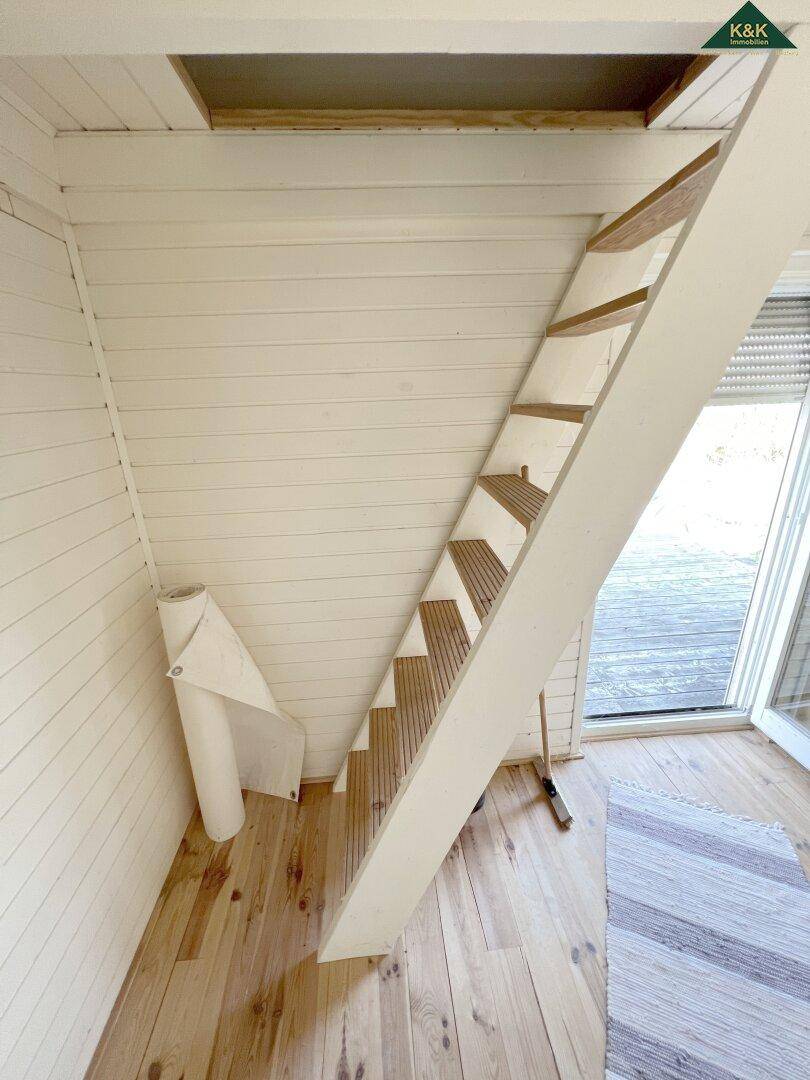 Steile Holztreppe führt zu einem oberen Bereich, umgeben von hellen Holzvertäfelungen und Holzboden.