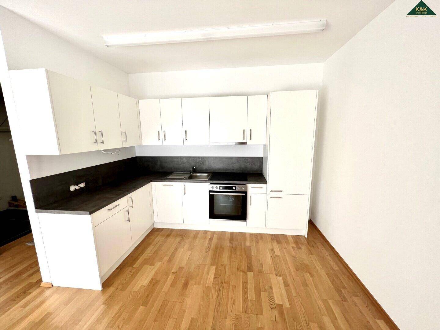Leere Küche mit weißen Einbauschränken, dunkler Arbeitsplatte und Holzboden.