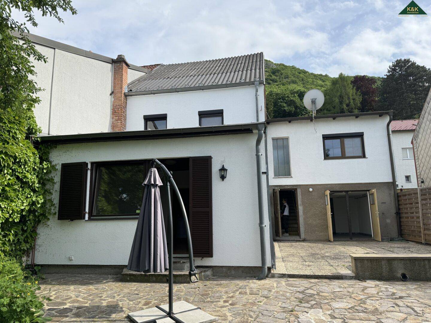 Hinterhof mit gepflasterter Terrasse, Sonnenschirm und Blick auf die Hügel.