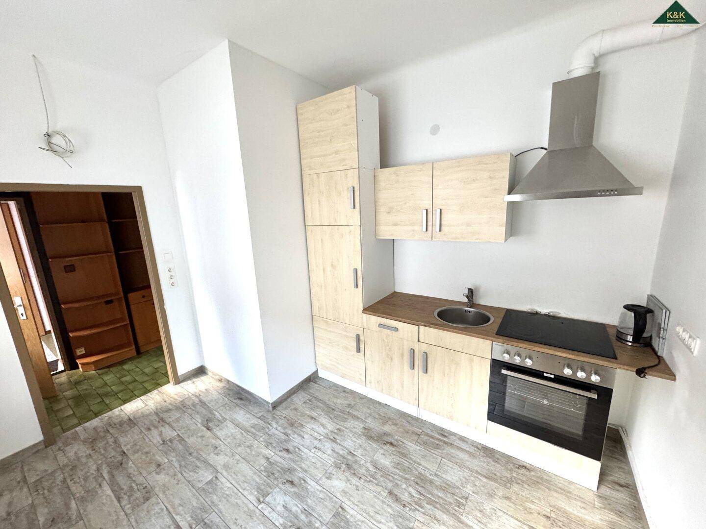 Kleine Einbauküche mit hellen Holzfronten, Spüle und Kochfeld.