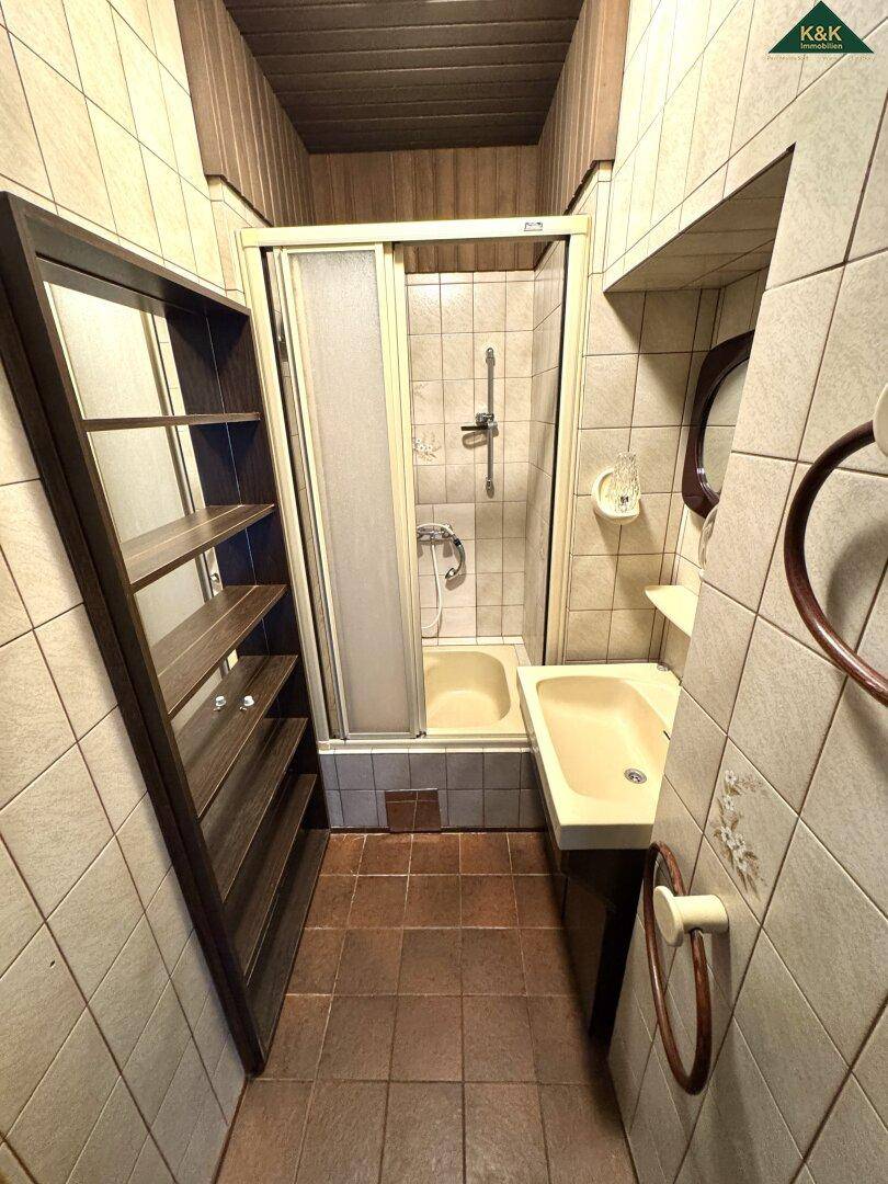 Kleines Badezimmer mit Duschkabine, Waschbecken und beigefarbenen Fliesen.