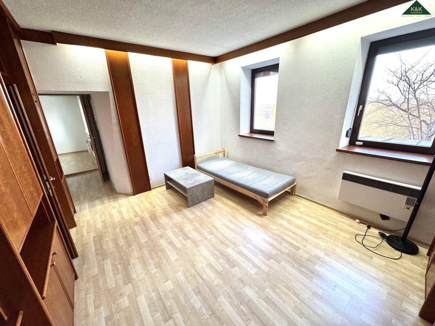 Schlafzimmer mit Laminatboden, zwei Fenstern und Blick in den Flur.
