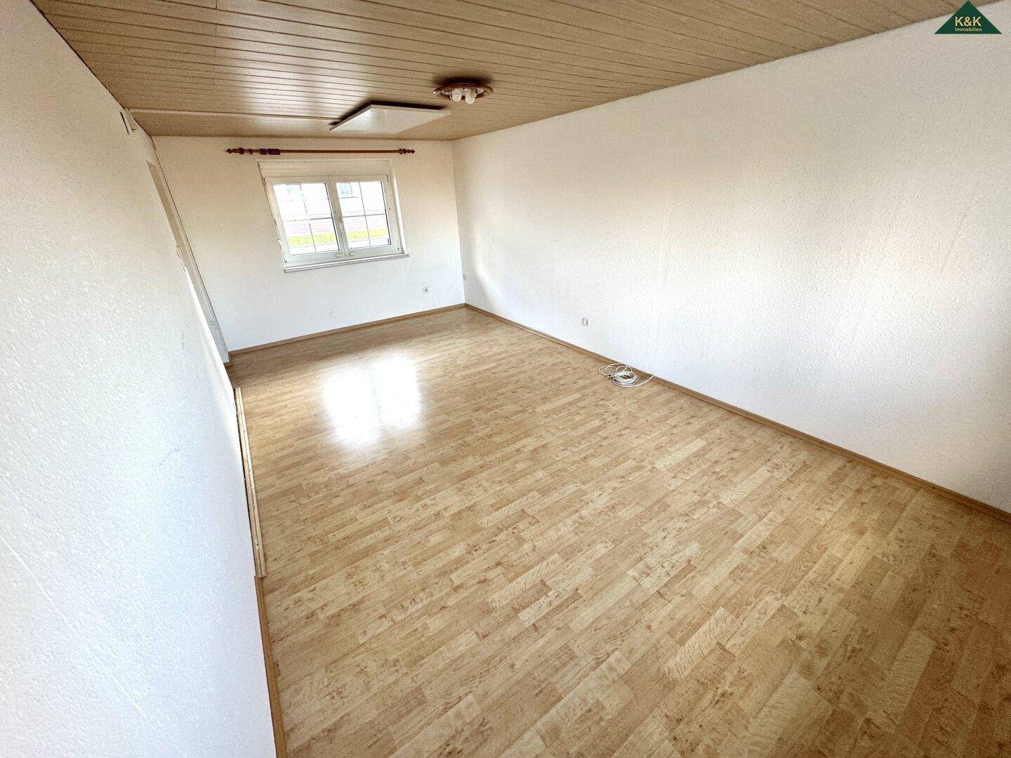 Leeres Zimmer mit Laminatboden, Holzdecke und einem Fenster.