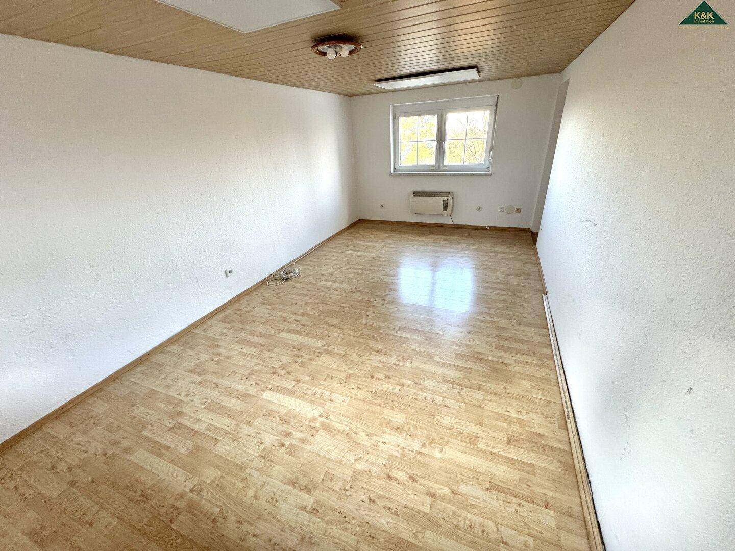 Heller Raum mit Laminatboden, Holzdecke und Heizkörper unter dem Fenster.