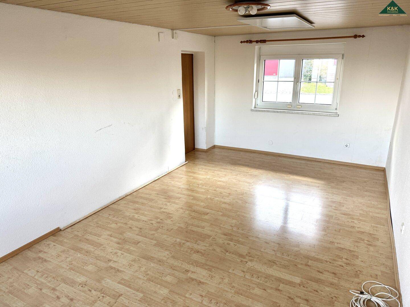 Geräumiges Zimmer mit Laminatboden, weiß gestrichenen Wänden und Holztür.