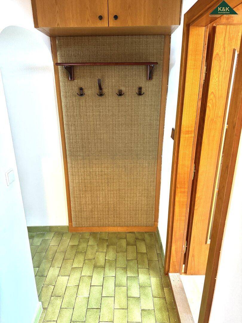 Eingangsbereich mit grünen Fliesen, Garderobe und Holzverkleidung.