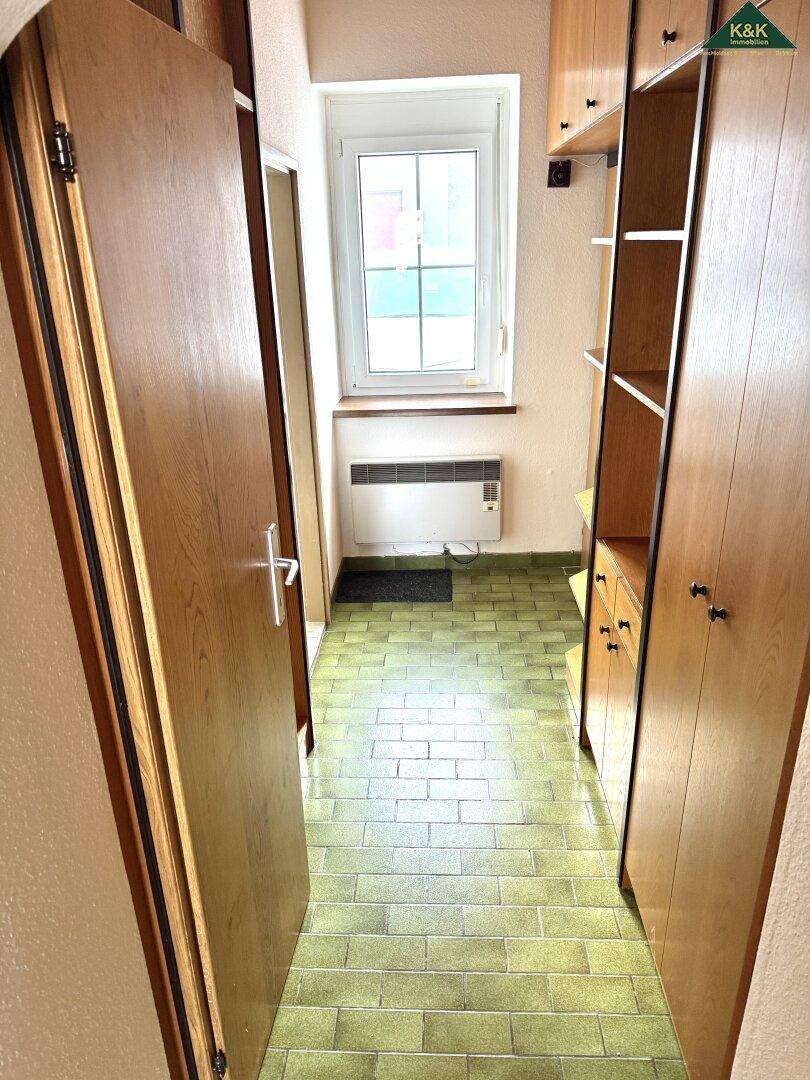 Langer Flur mit grünen Fliesen, Einbauschränken und Fenster am Ende.
