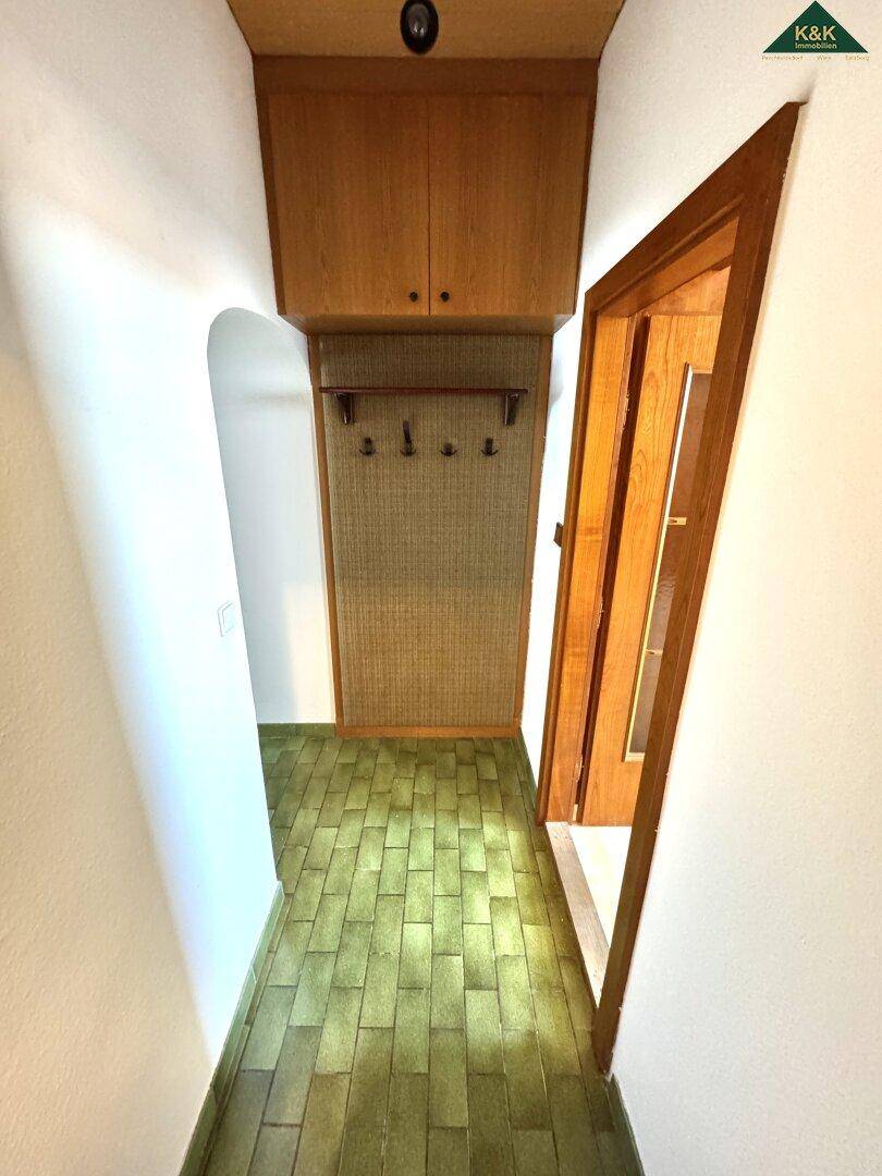 Eingangsbereich mit grünen Fliesen, Garderobe und Holzverkleidung.