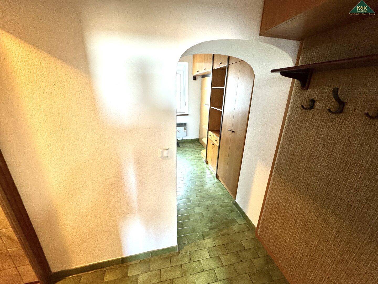 Flur mit grünen Fliesen, Garderobe und Blick in den hinteren Bereich.