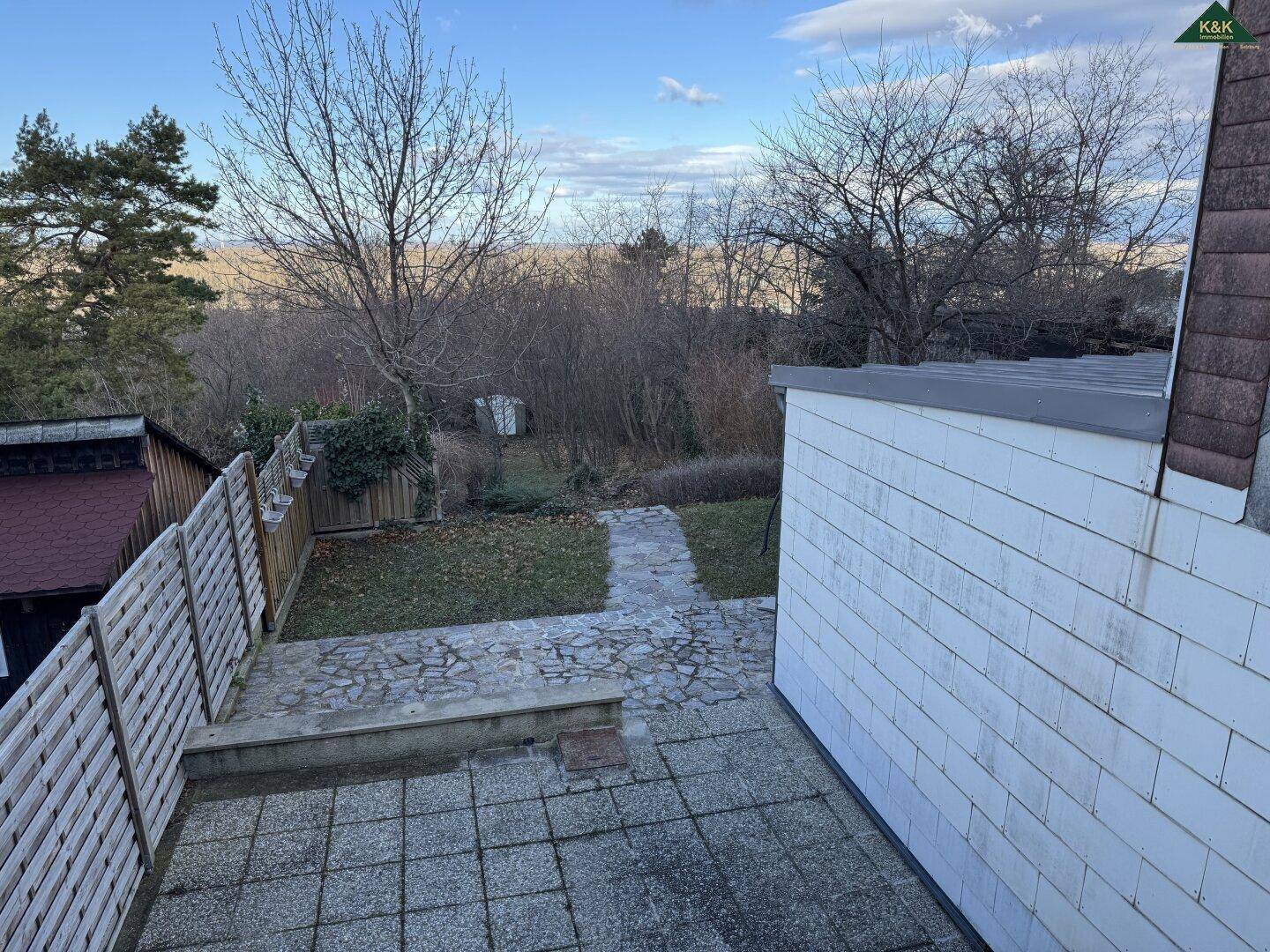 Gartenbereich mit gepflasterter Terrasse, einem Steinweg und weitem Blick in die Landschaft.