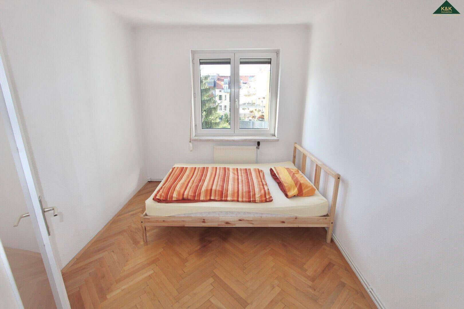 Helles Schlafzimmer mit Holzbett, weiß gestrichenen Wänden und klassischem Fischgrätparkettboden.