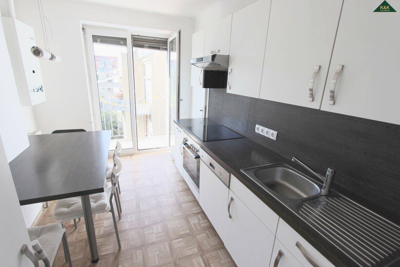 Helle Küche mit weißer Einbauküche, dunkler Arbeitsplatte und direktem Zugang zum Balkon.