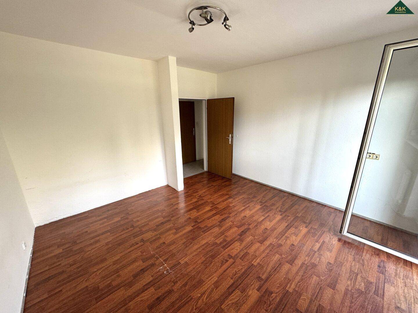 Geräumiges Zimmer mit Laminatboden und Zugang zu weiteren Räumen, vielseitig nutzbar.