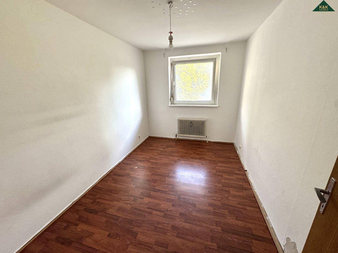Kleineres Zimmer mit dunklem Laminatboden und Fenster, geeignet als Schlaf- oder Kinderzimmer.