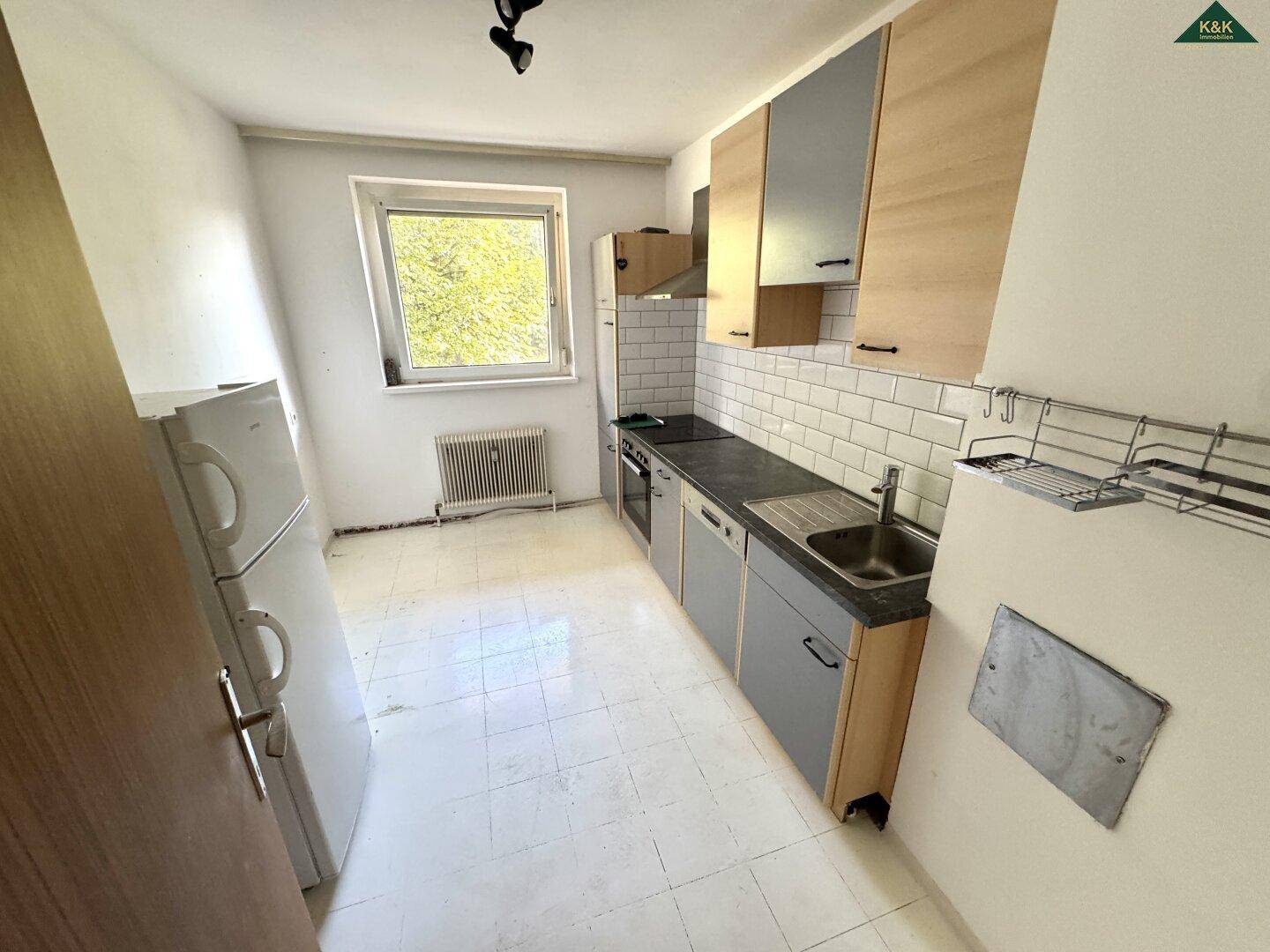 Helle Küche mit Fenster, Fliesenboden und integrierten Geräten, bietet praktischen Arbeitsbereich.