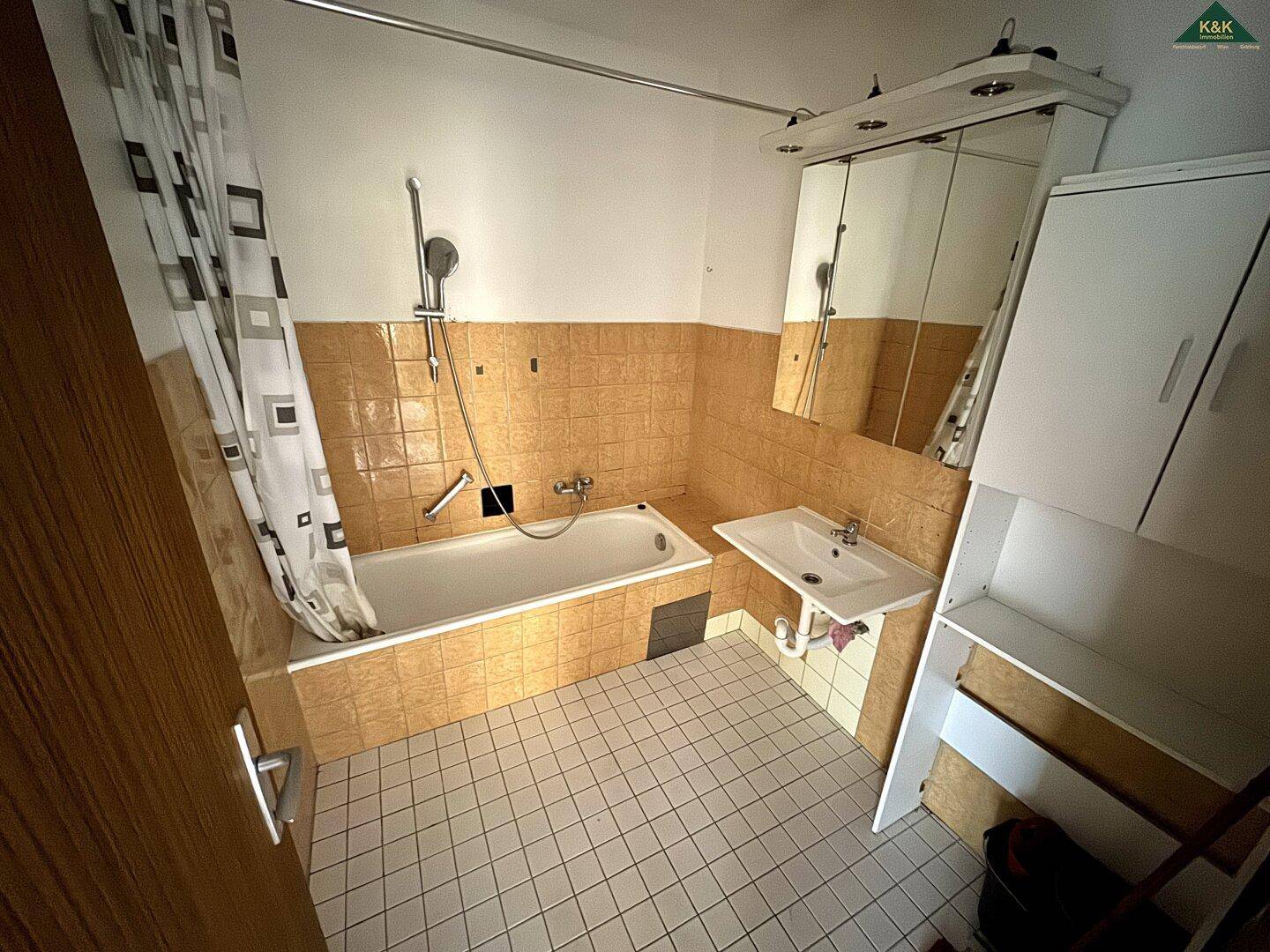 Badezimmer mit Badewanne, Waschbecken und Spiegelschrank, gefliest in warmen Orangetönen.