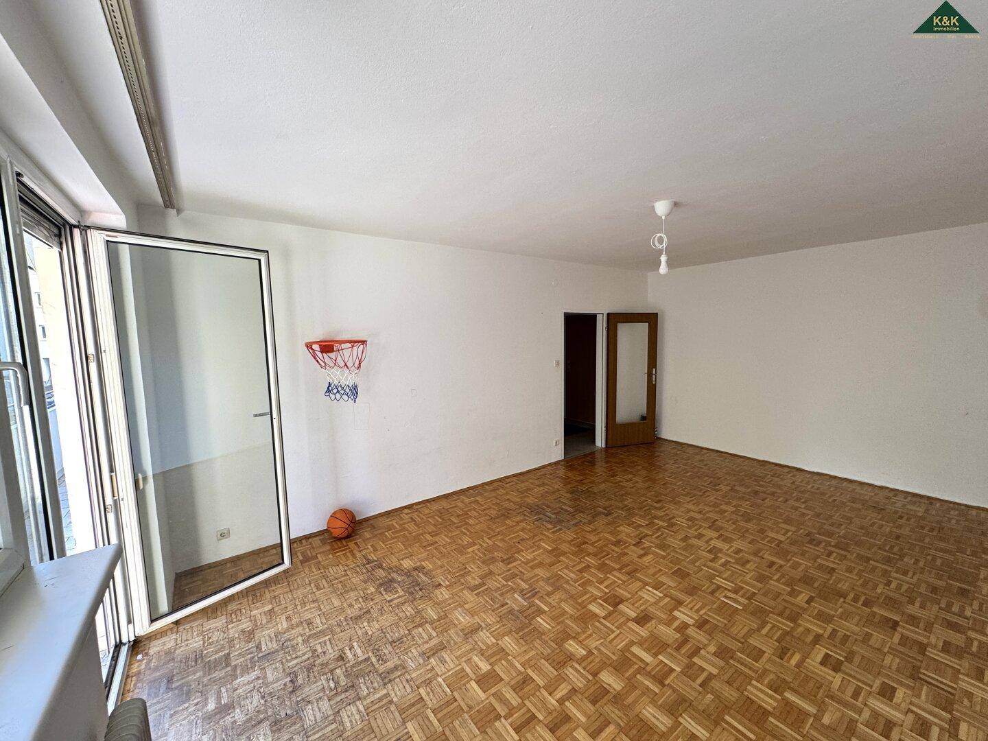Heller Wohnbereich mit Parkettboden und breiter Balkontür, bietet viel Tageslicht.