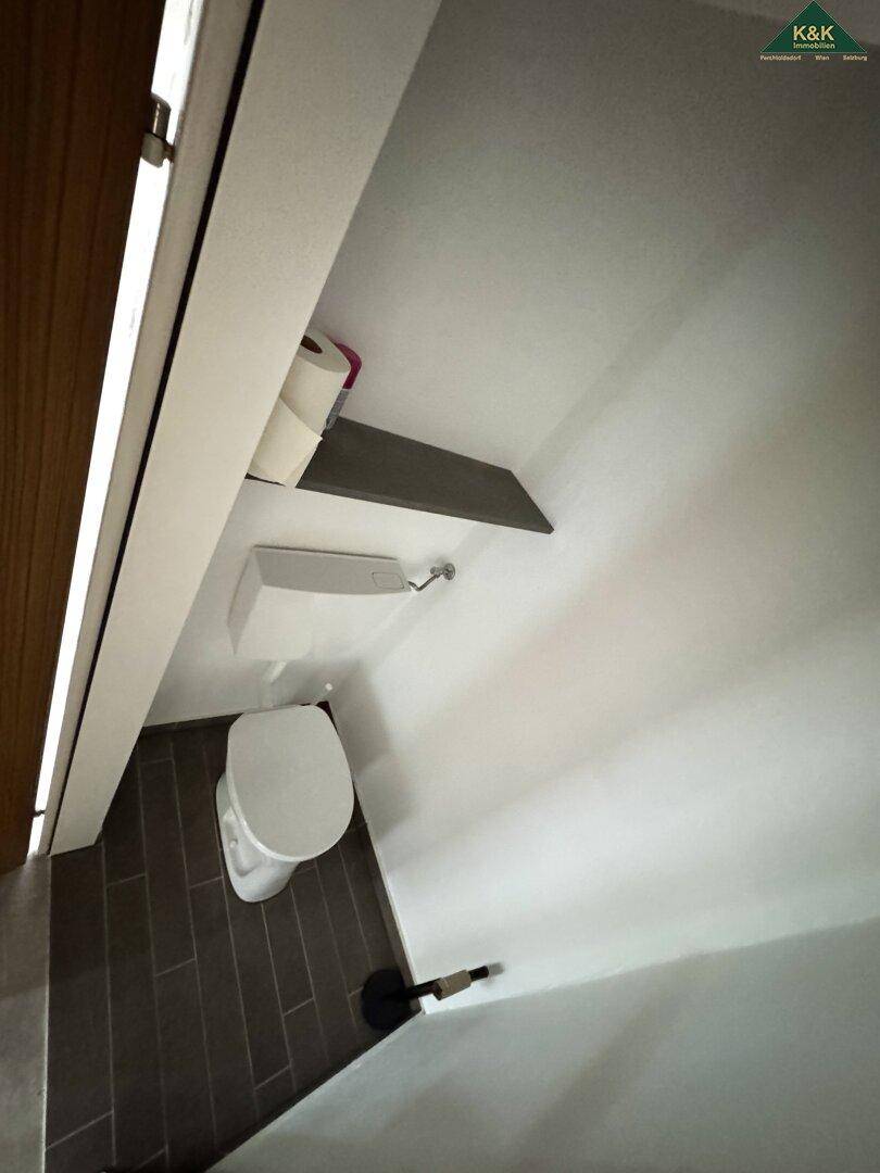 Kleines separates WC mit Wandtoilette und dunklem Fliesenboden, minimalistisch gestaltet.