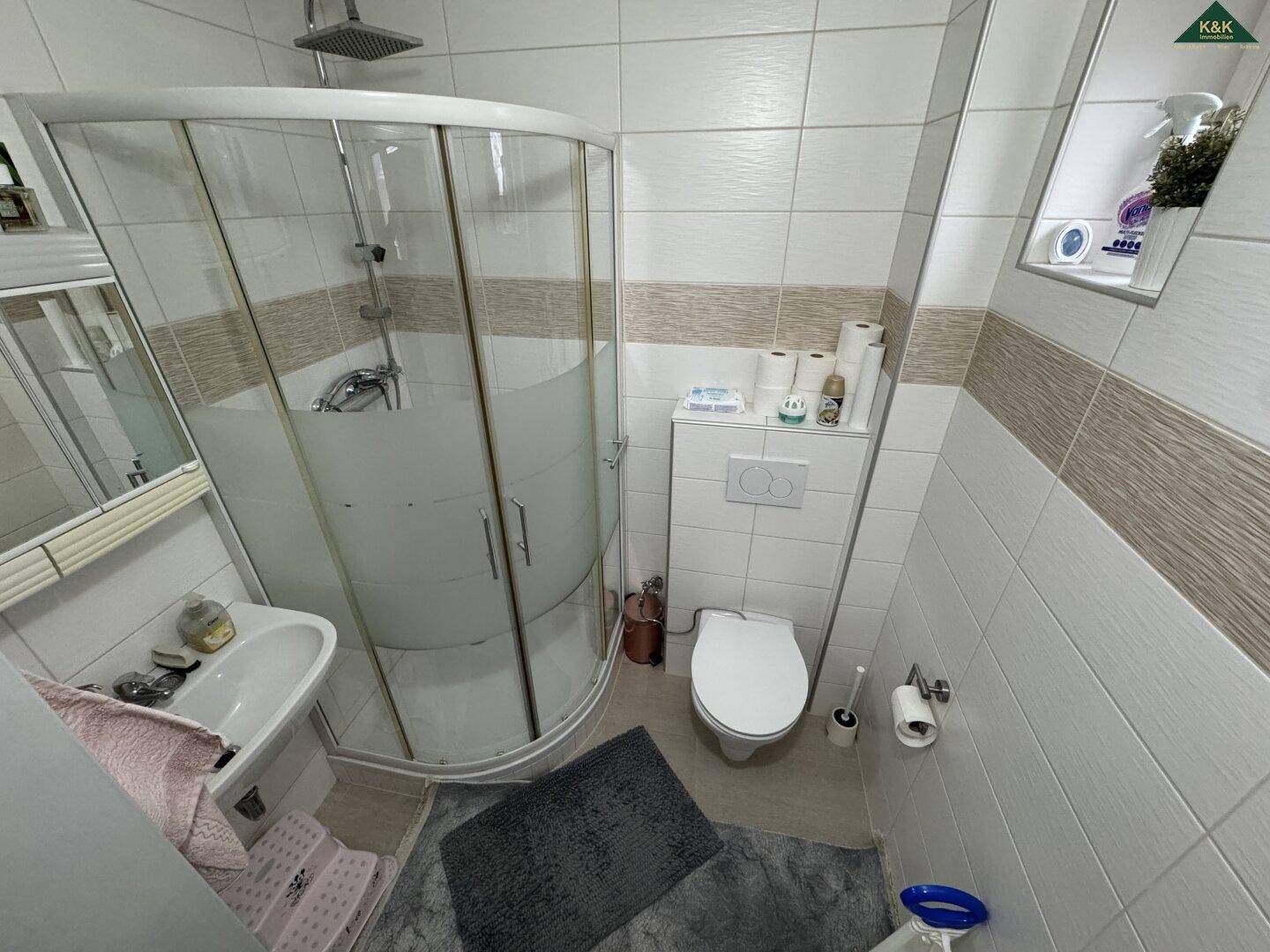 Helles Badezimmer mit Eckdusche, WC und Waschbecken, komplett gefliest in neutralen Farben.