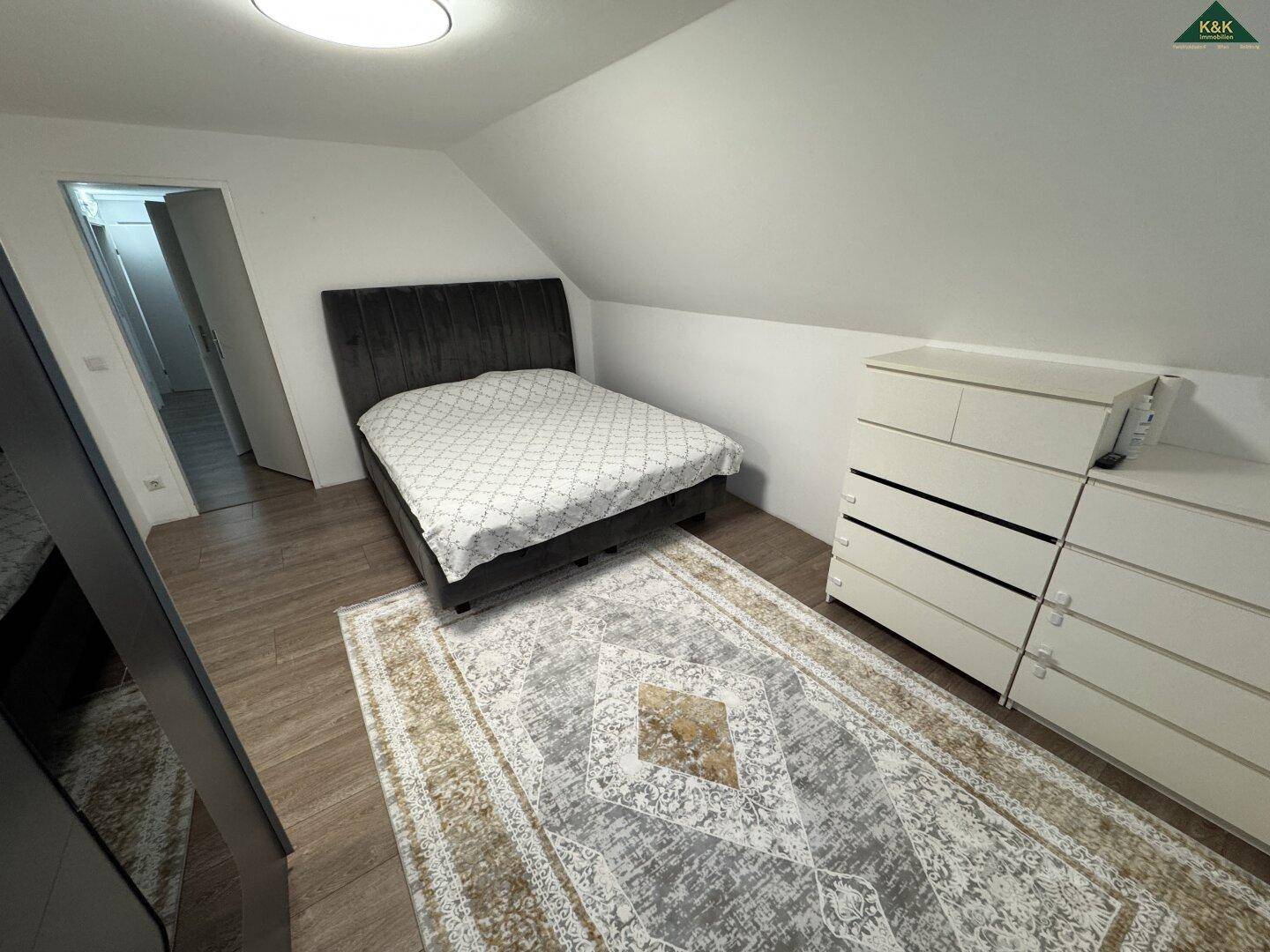 Schlafzimmer mit Bett und Kommode unter einer Dachschräge, ausgestattet mit Laminatboden.