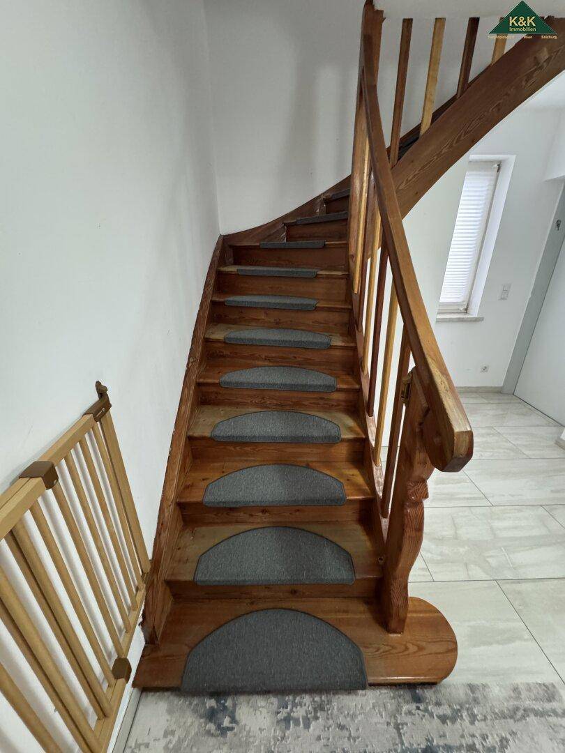 Detailansicht der Holztreppe mit Teppichstufen und Kinderschutzgitter.