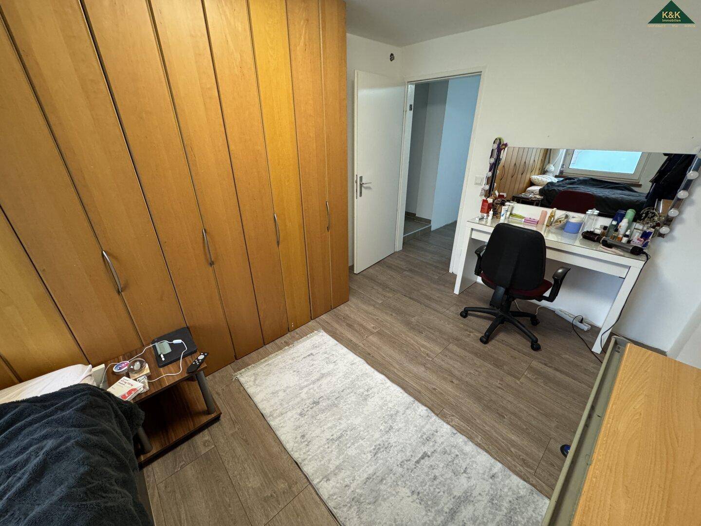 Schlafzimmer mit großem Holzschrank, Schminktisch und Blick auf den Außenbereich.