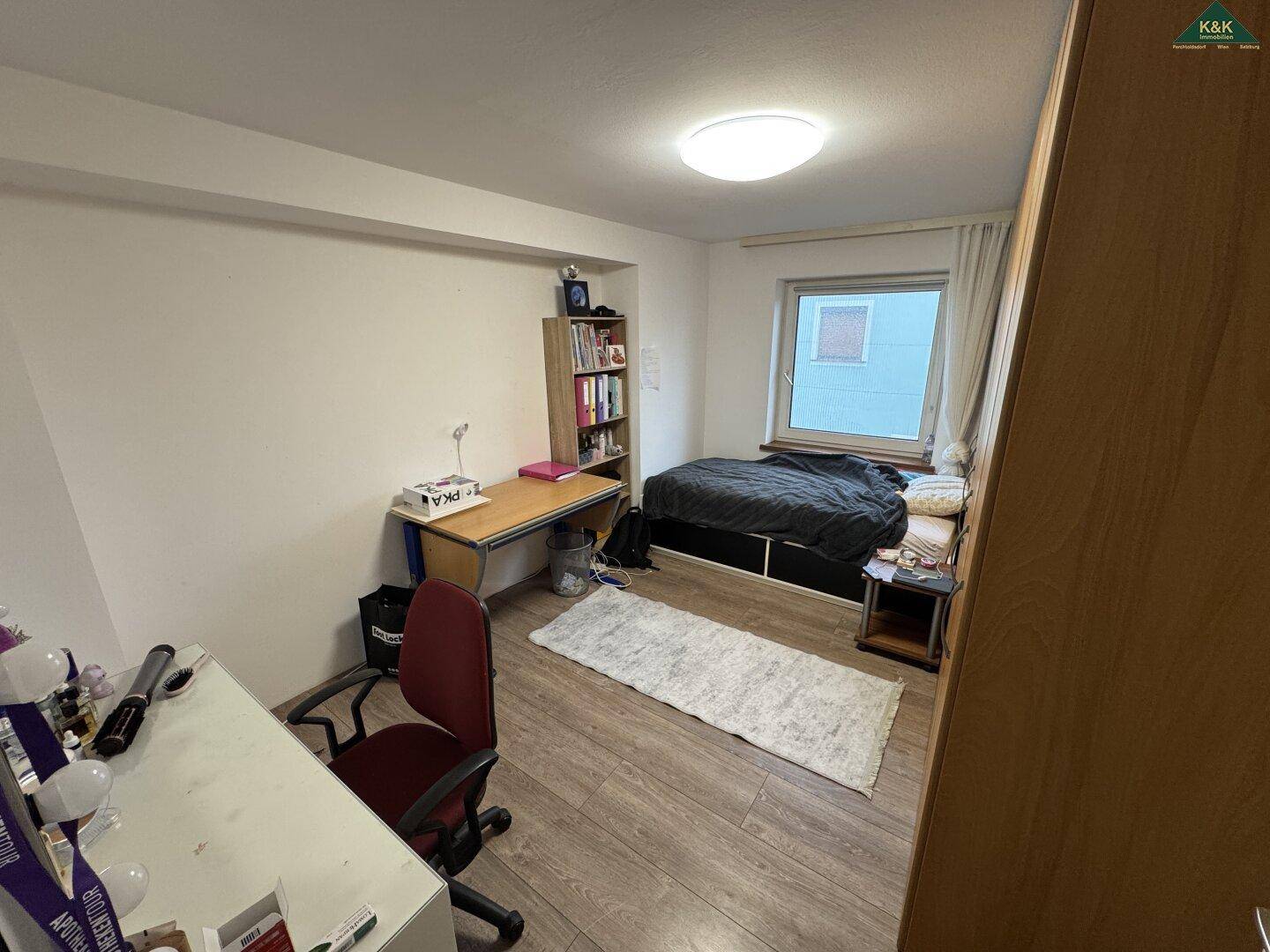 Jugendzimmer oder Büro mit Bett, Schreibtisch und Bücherregal am Fenster.