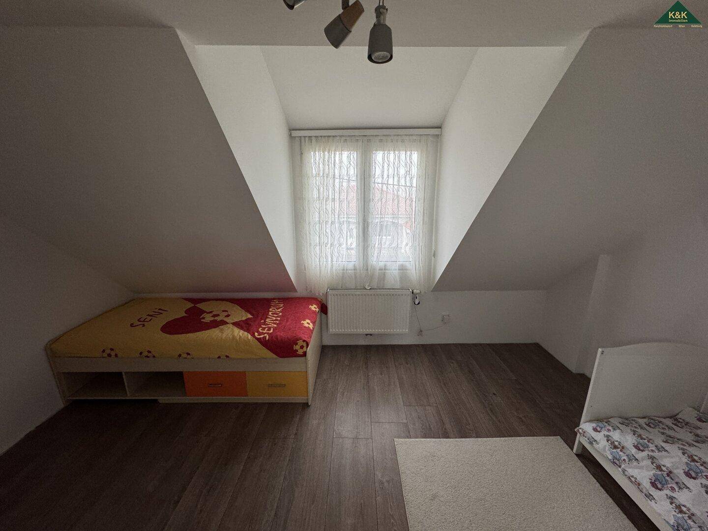 Kinderzimmer im Dachgeschoss mit zwei Betten, schrägen Wänden und Fenster.