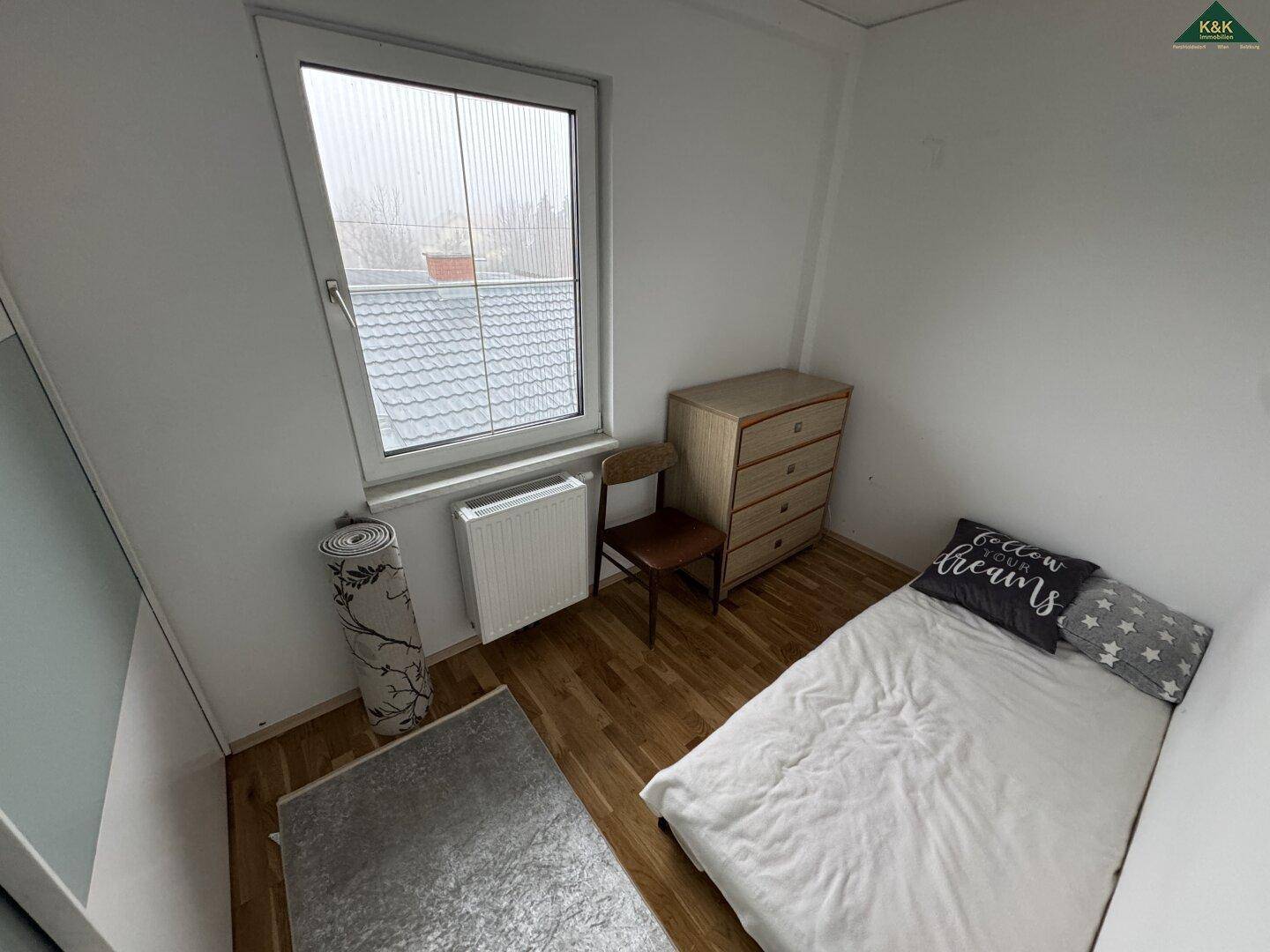 Kleines Schlafzimmer mit Einzelbett, Kommode und Fenster mit Blick nach draußen.