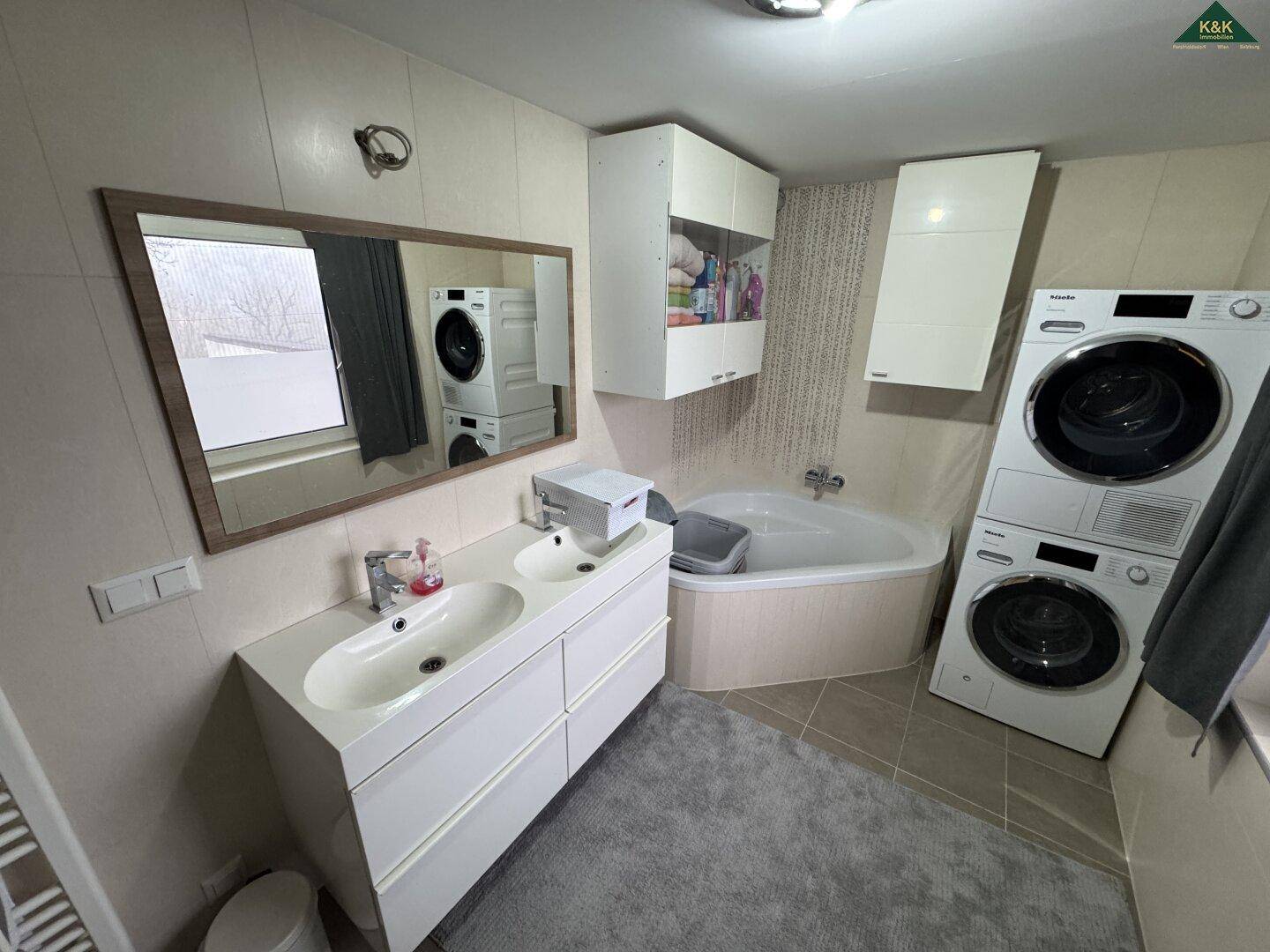 Modernes Badezimmer mit Doppelwaschbecken, Badewanne und Waschmaschine.