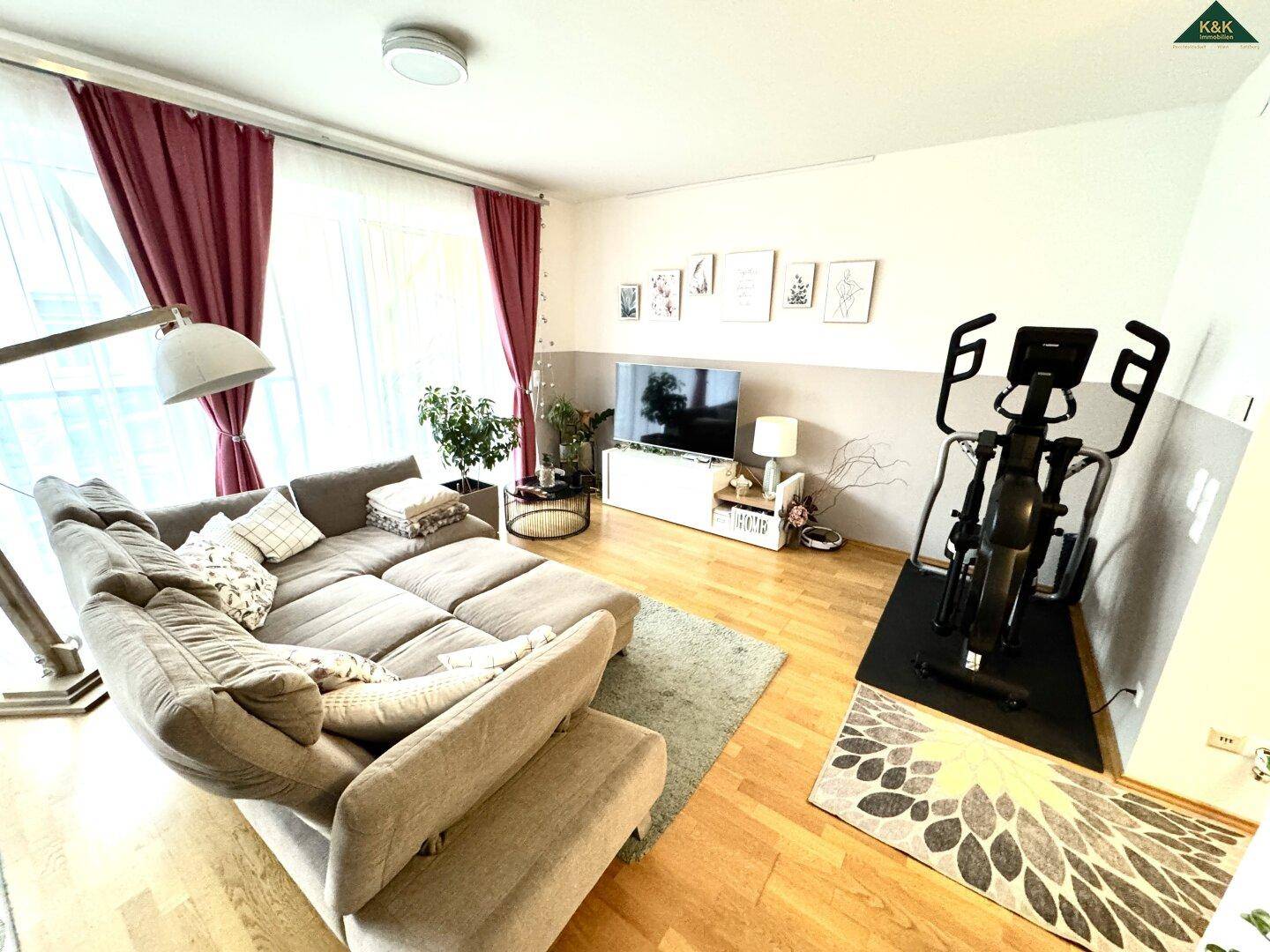 Gemütliches Wohnzimmer mit großem Sofa, Holzboden und einem Bereich für Fitnessgeräte.