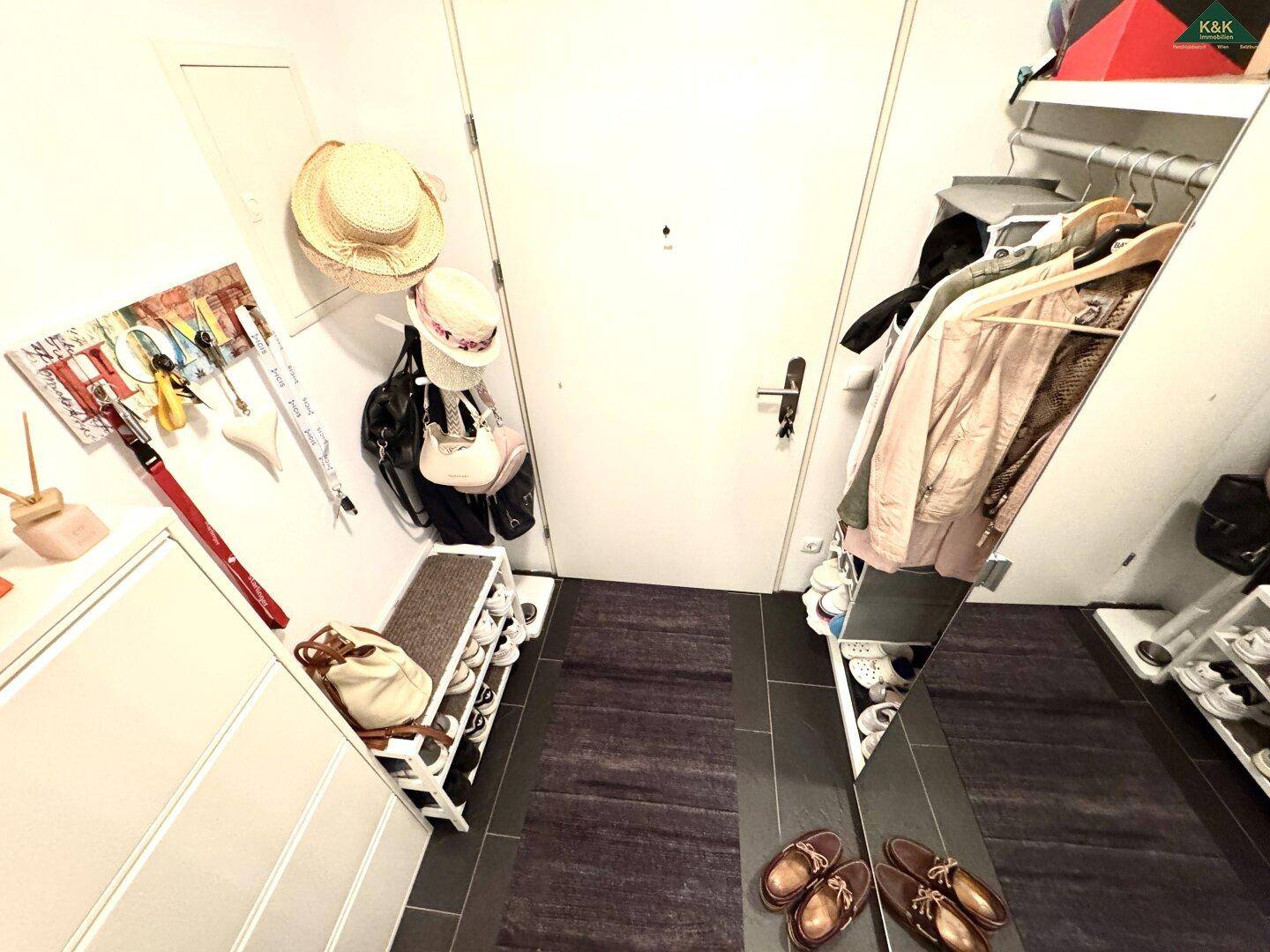 Eingangsbereich mit praktischen Schuhregalen und Garderobe auf dunklem Fliesenboden.