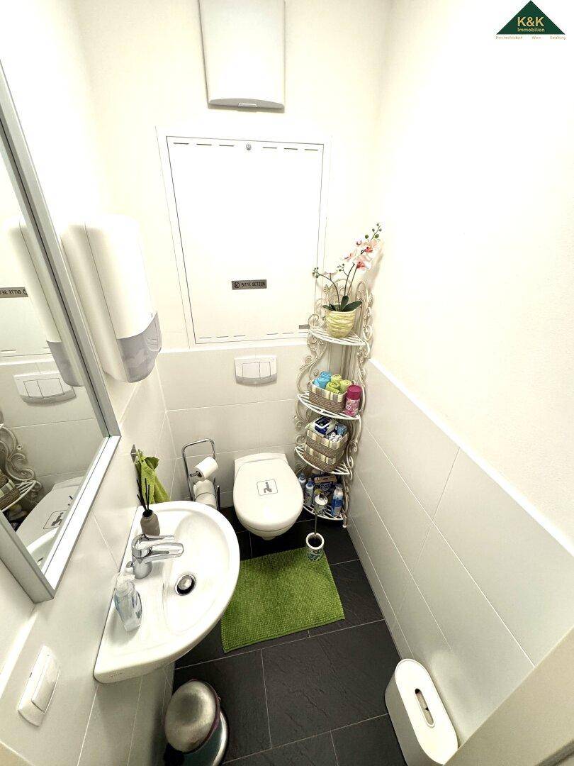 Kleines Gäste-WC mit Waschbecken und Toilette, ausgestattet mit weißen Wandfliesen.