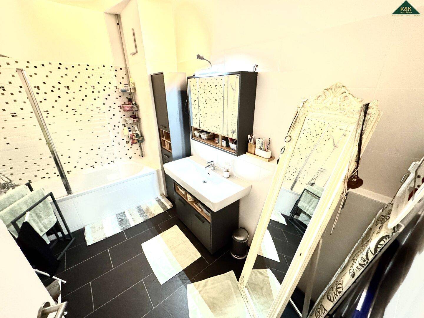 Modernes Badezimmer mit Badewanne, Duschwand, Einzelwaschbecken und großem Spiegel.