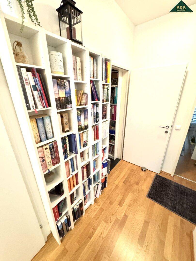 Heller Flur mit einem hohen, gut gefüllten Bücherregal und warmem Holzboden.